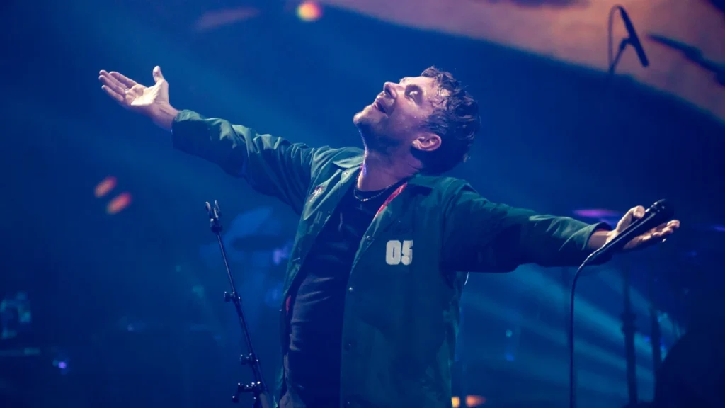 Damon Albarn on stage with arms outstretched under blue light