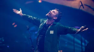 Damon Albarn on stage with arms outstretched under blue light