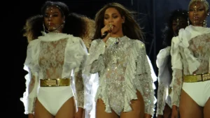Beyonce singing into a microphone on stage flanked by dancers